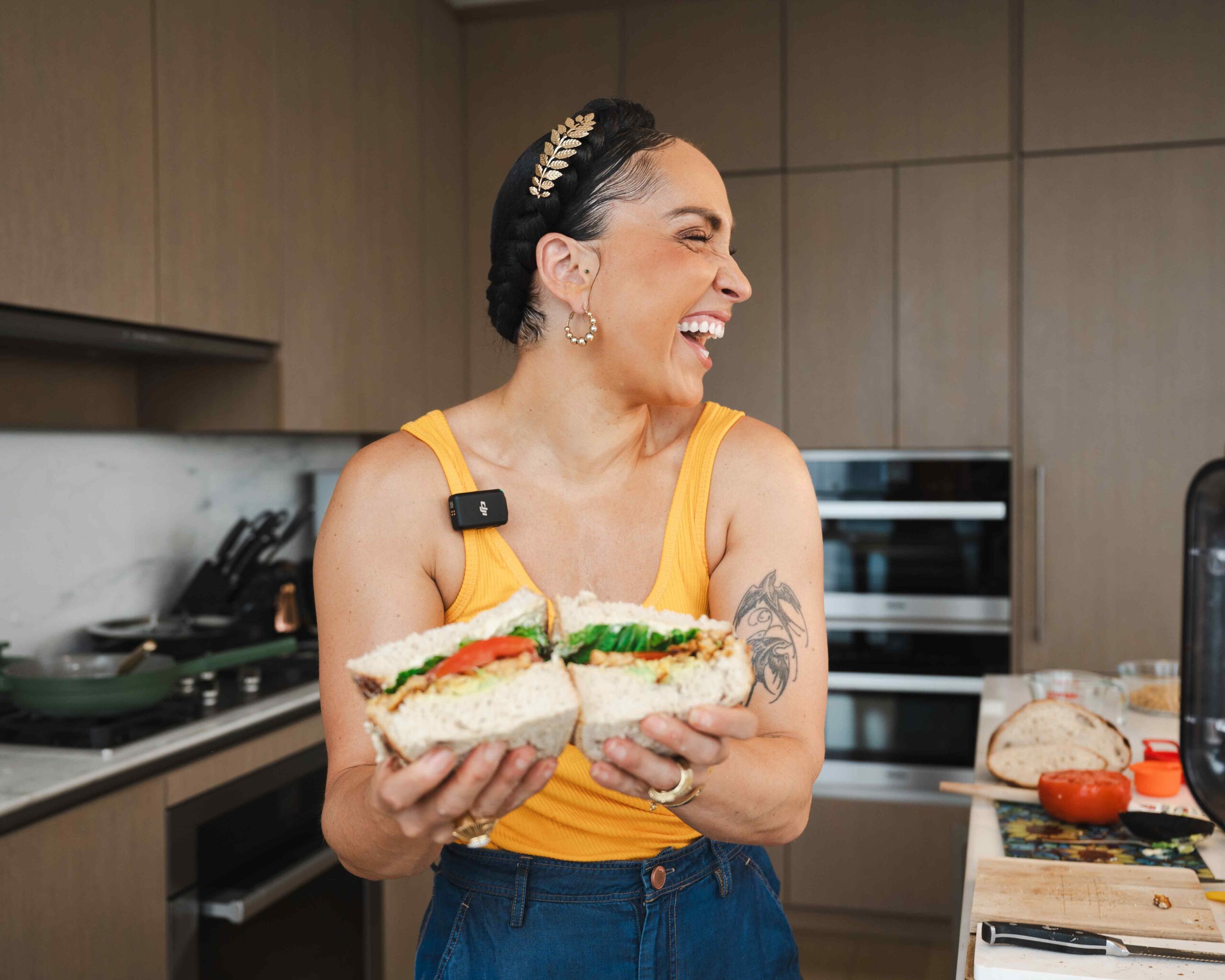 Head Peloton instructor Robin Arzón, a vegan, holds up a plant-based TLT sandwich in her kitchen and looks to the side, laughing