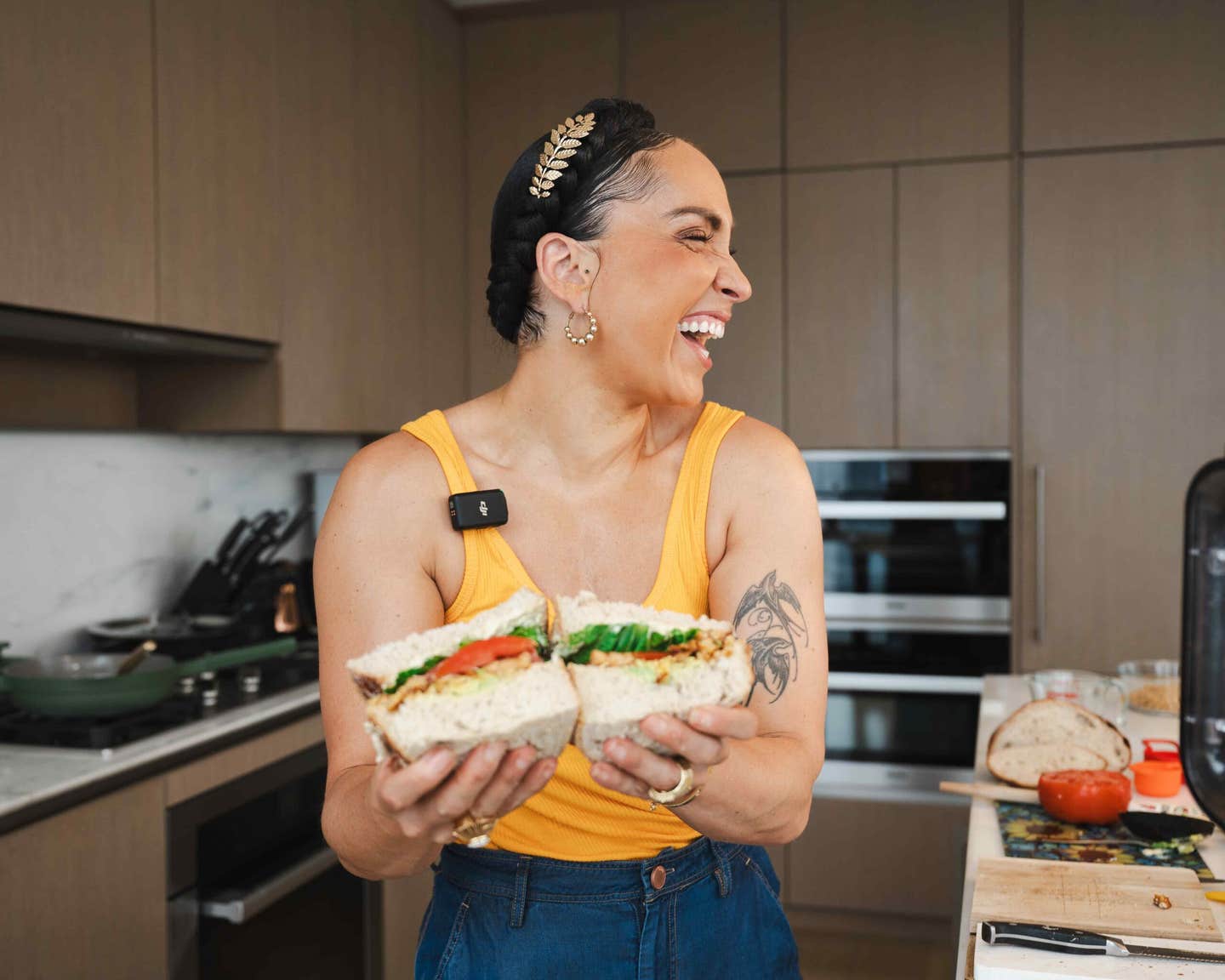Head Peloton instructor Robin Arzón, a vegan, holds up a plant-based TLT sandwich in her kitchen and looks to the side, laughing