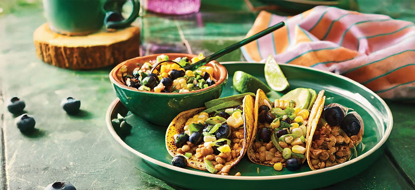 Three Lentil Tacos with Blueberry Corn Salsa on a green plate next to a small bowl of salsa