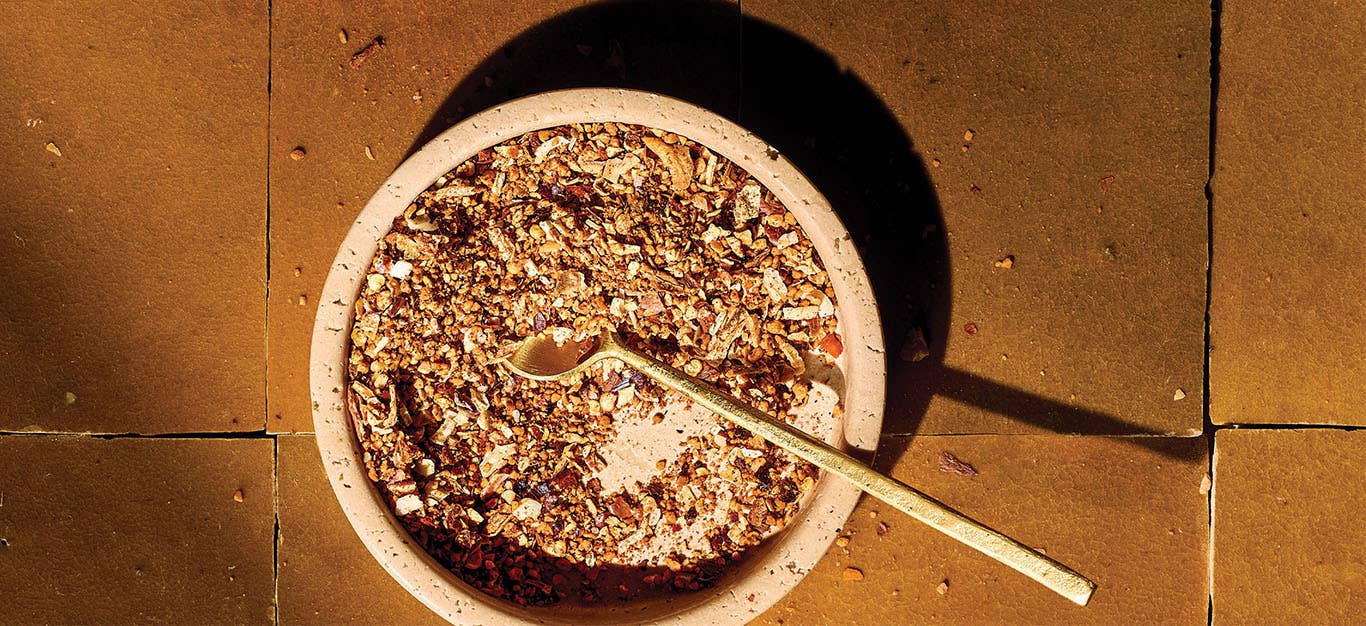 An earthy tile background and a ceramic bowl of Oil-Free Chili Crisp with a long-handled teaspoon in the bowl