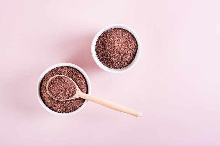 Kala namak (Black Himalayan salt) in bowl with wooden spoon on pale pink background
