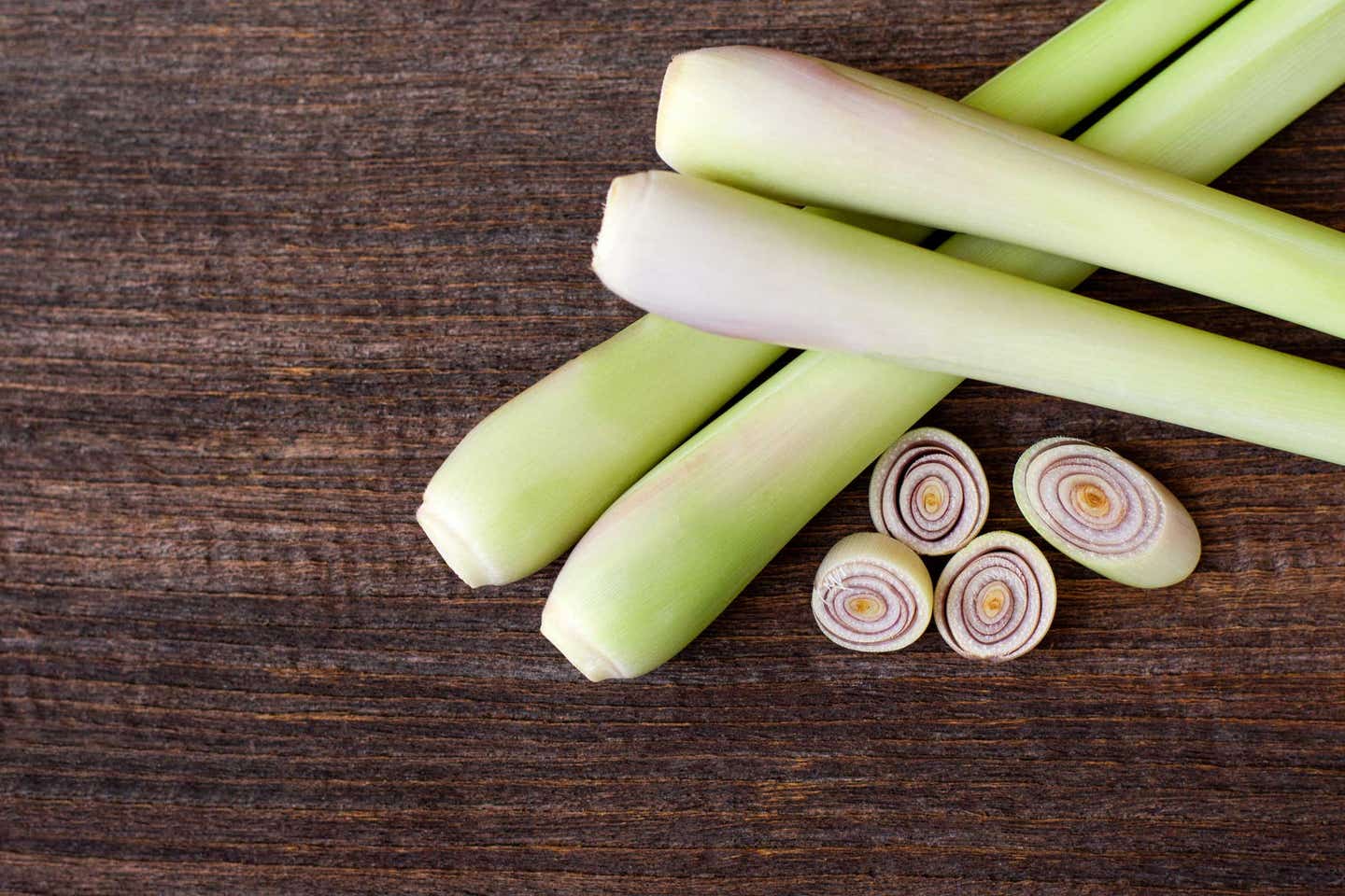 Four stalks of lemongrass shown close up, with a few rounds of sliced lemongrass lying beside them