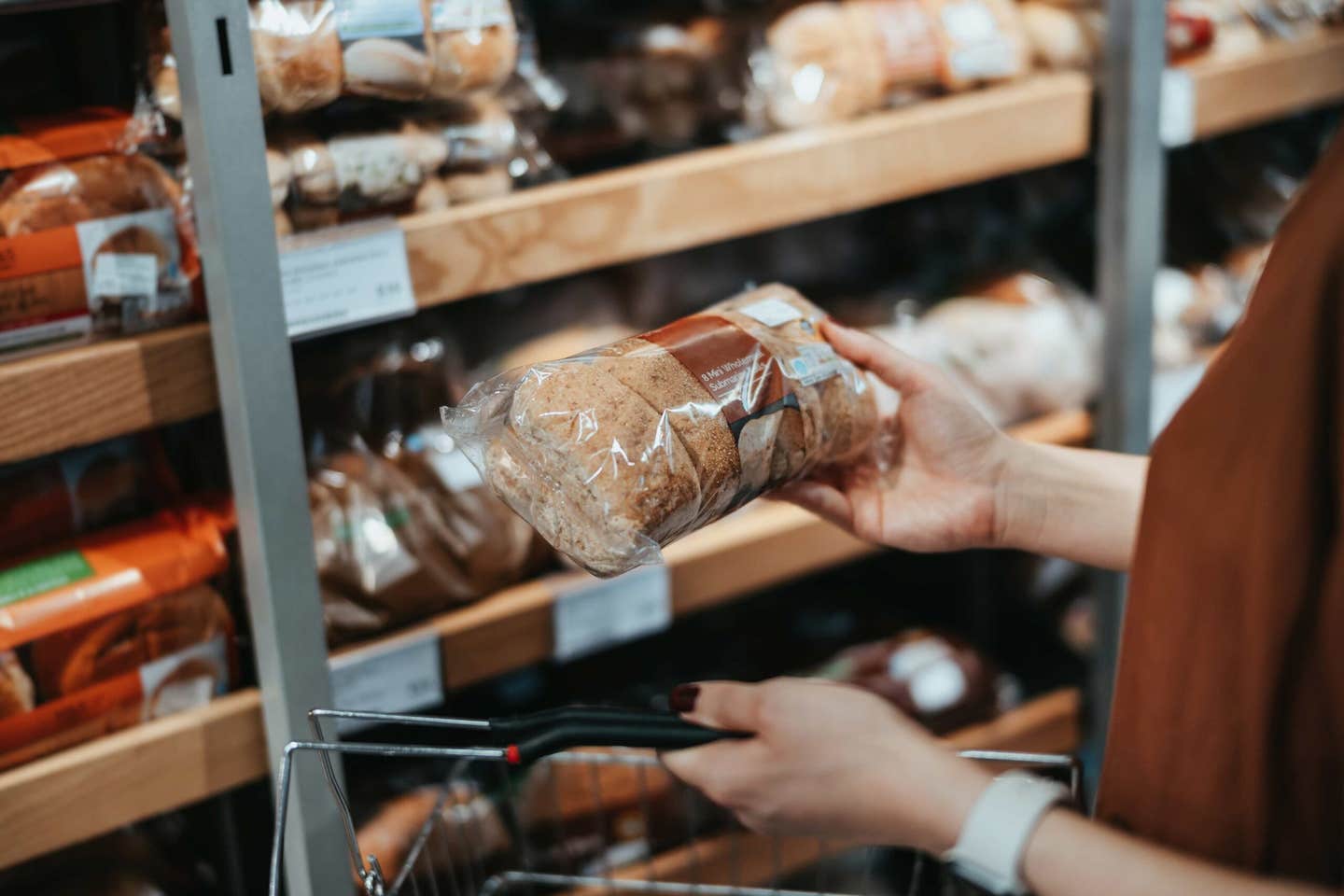 A woman's hand holding up a whole grain loaf of bread at the grocery store, reading the label