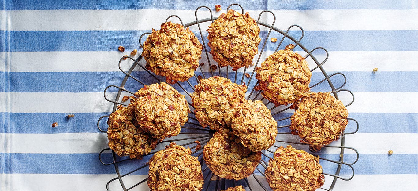 A cooling track piled high with Banana Oat Cookies, over a blue and white striped dish towel