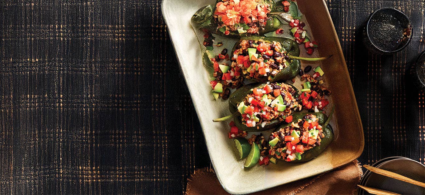 Four Chipotle Black Bean and Rice Stuffed Poblanos in a casserole dish resting on a black checkered cloth