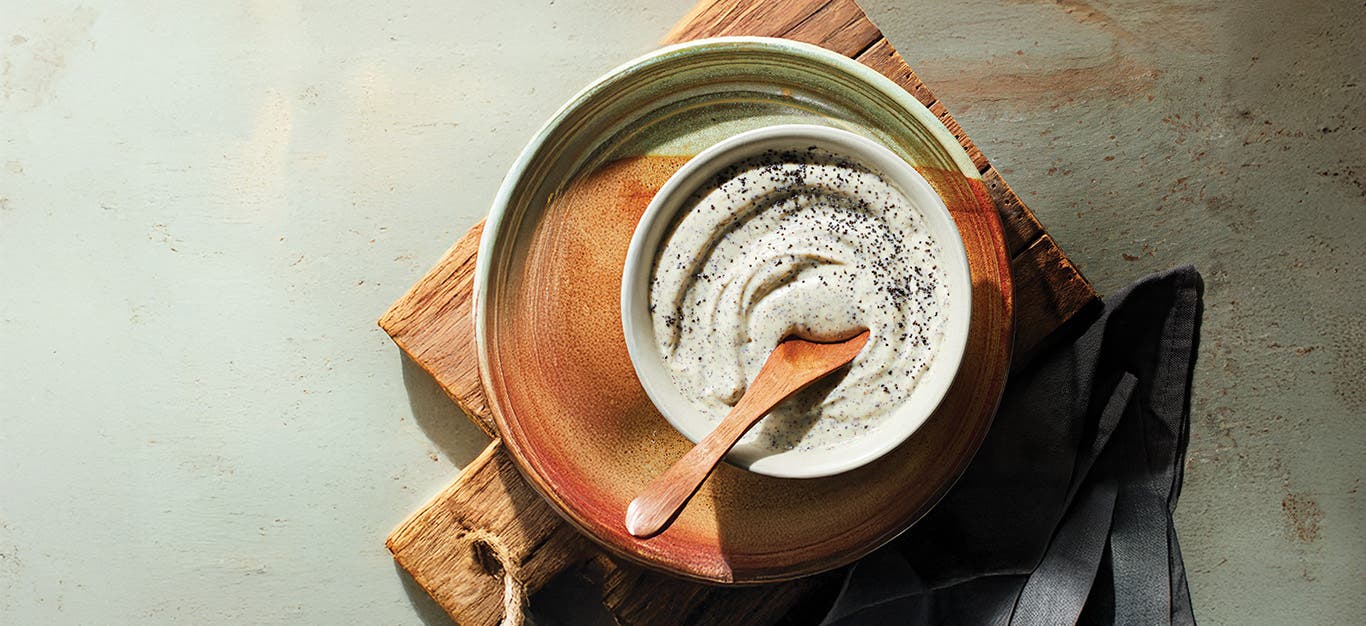 A rustic bowl of creamy poppy seed dressing on a n earthy handmade ceramic plate on a wooden chopping board