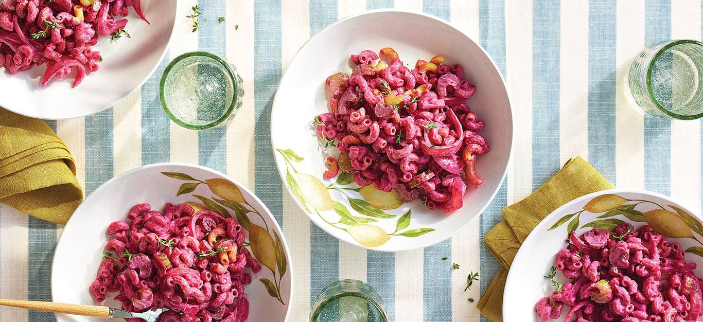 Four white bowls of Easy, Creamy Beet Pasta on a pale blue and white striped table cloth
