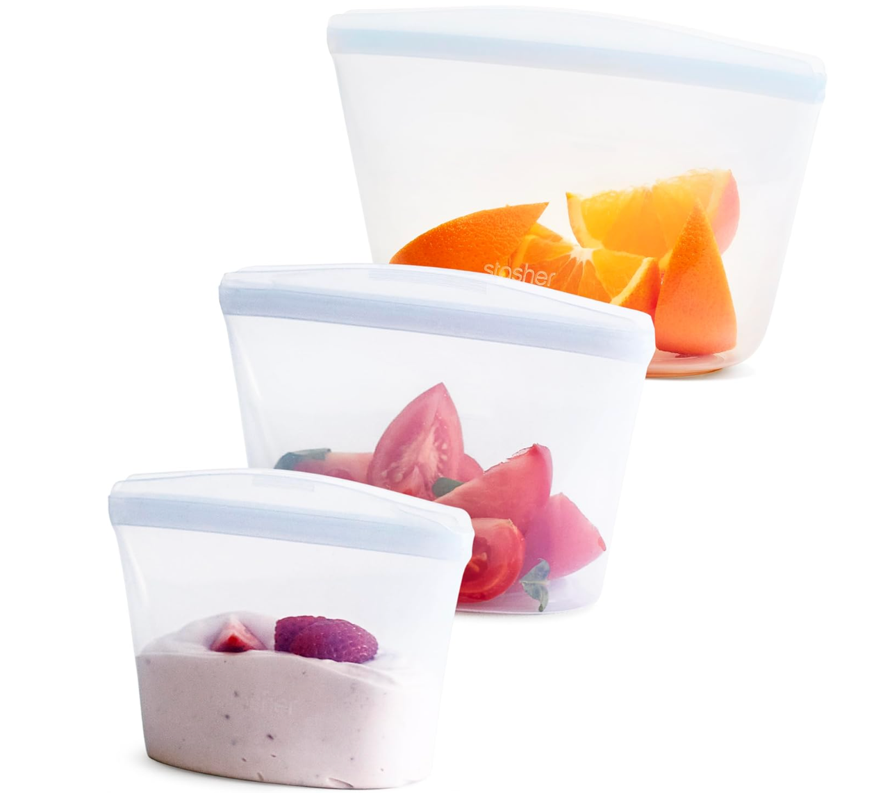three clear Stasher bags of different sizes, with a selection of fruits and tomatoes in each