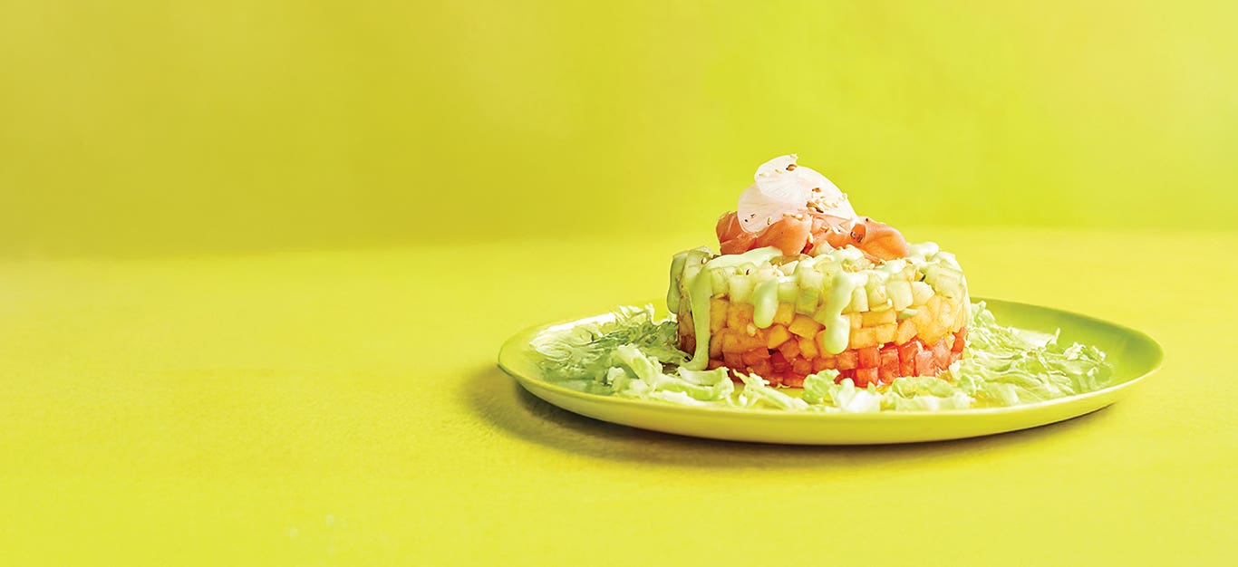 A plate with one Melon Poke Stack with Avocado-Wasabi Drizzle against a bright yellow-green background