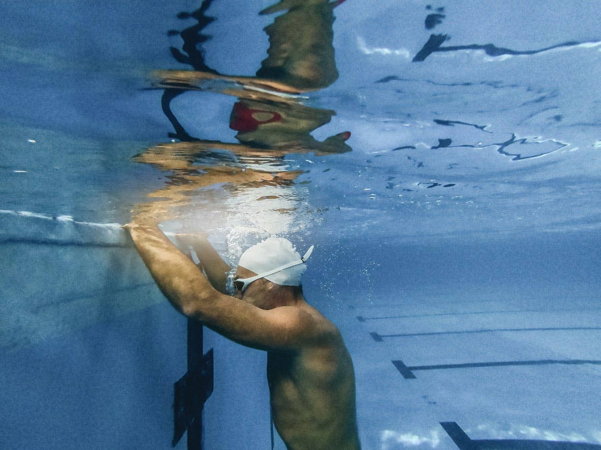 An athletic man submerged underwater in a pool blows out bubbles in a breathing exercise for swimming
