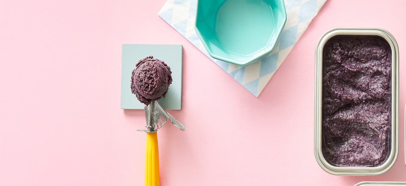 A scoop of Adzuki Bean Nice Cream next to a stainless steel container of the ice cream against a pale pink background
