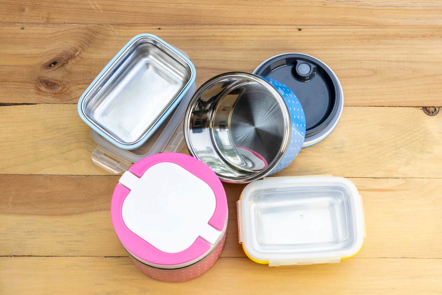 An array of stainless steel food containers with colorful lids on a wooden counter
