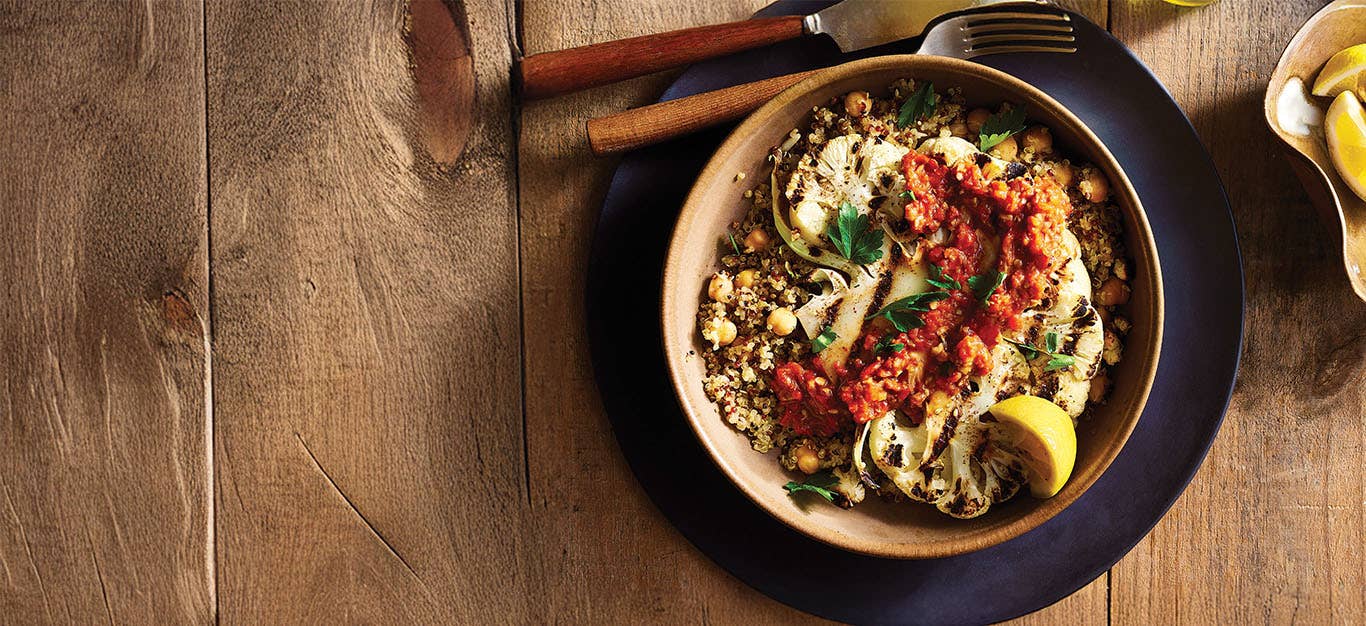 Grilled Cauliflower Steaks with Muhammara on an earthy brown plate on a dark wooden table top