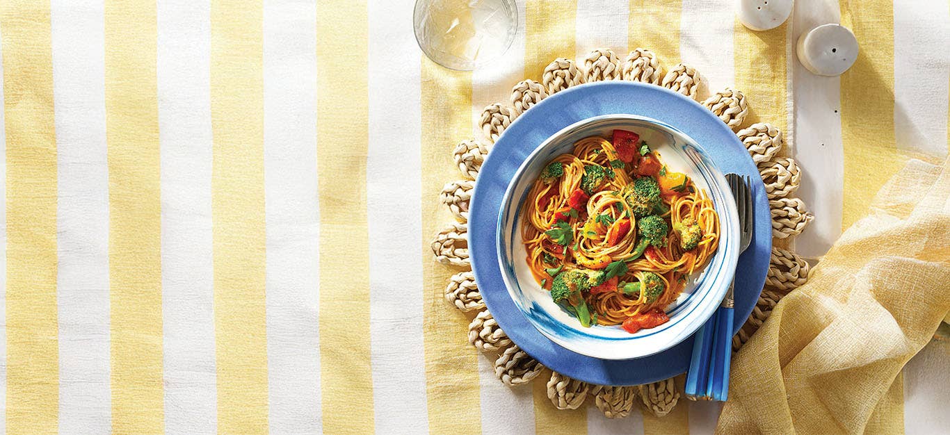 A blue ceramic bowl of Grilled Bell Pepper Pasta on a pale yellow and white tablecloth