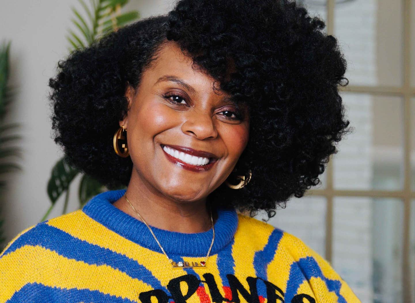Headshot of actress and vegan influencer Tabitha Brown wearing a colorful yellow and blue striped sweater