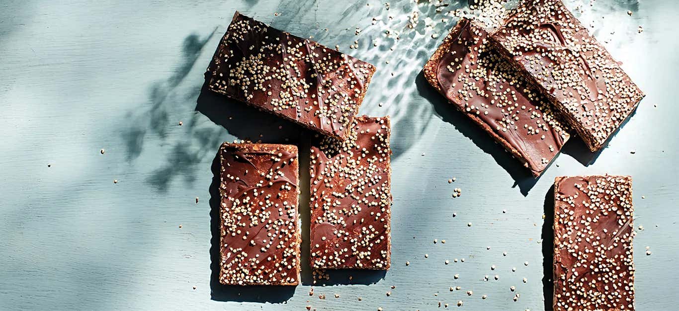 Six No-Bake Chocolate-Oat Energy Bars on a pale blue background, with grains of uncooked quinoa scattered around