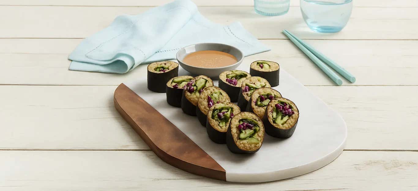 A wooden chopping board with sushi rolls and a small bowl of dipping sauce