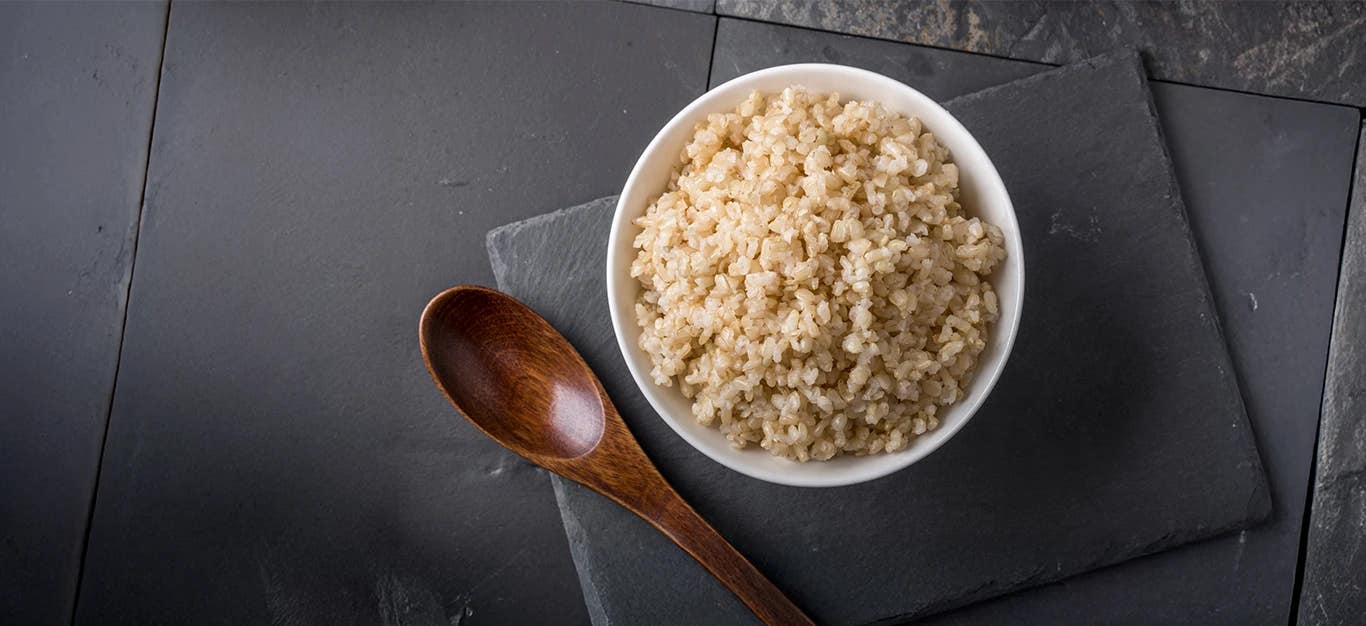 A bowl of Instant Pot Brown Rice against a dark grey background with a small wooden spoon beside the bowl
