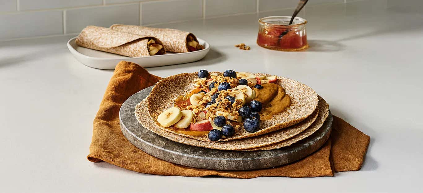 A whole grain tortilla topped with P B and J and topped with banana slices, berries, and granola