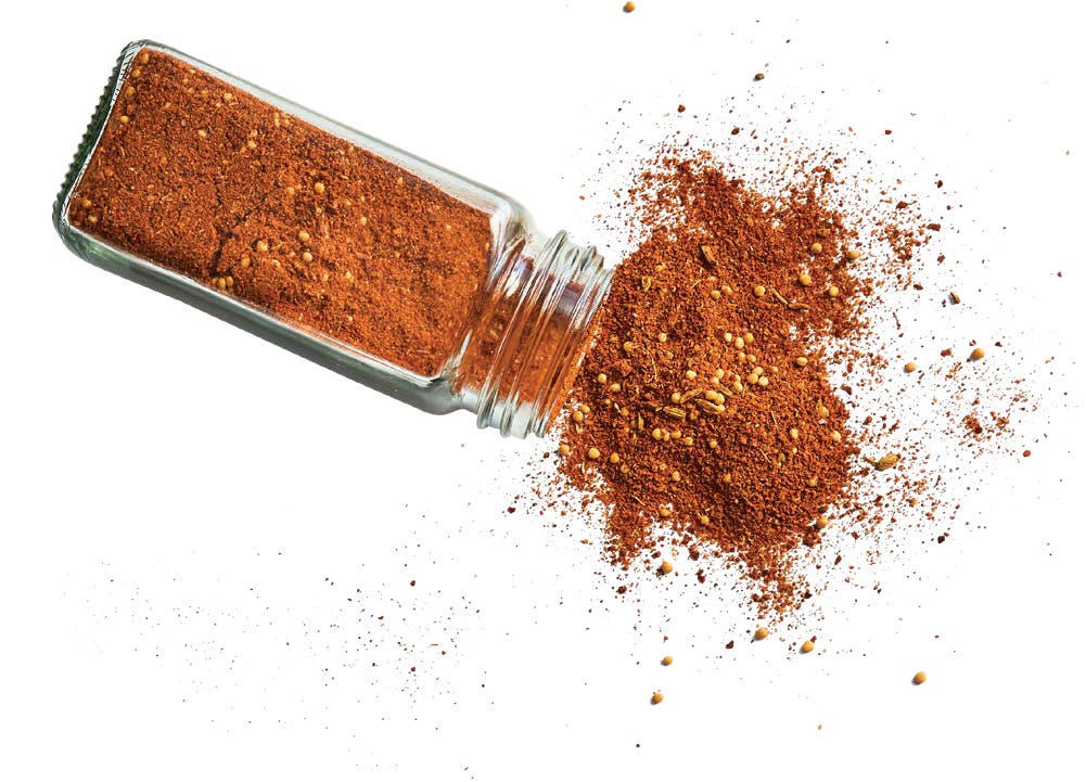 A clear glass jar of Pepperoni Seasoning rom the Local Spicery spilling out onto a white background f