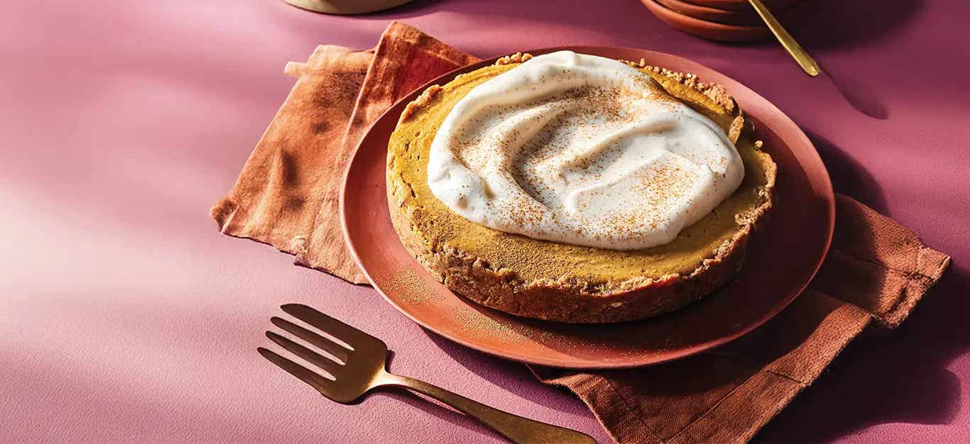 Vegan Pumpkin Cheesecake on a burnt orange plate, with a fork beside the plate and a large dollop of Aquafaba Whipped Cream on top.