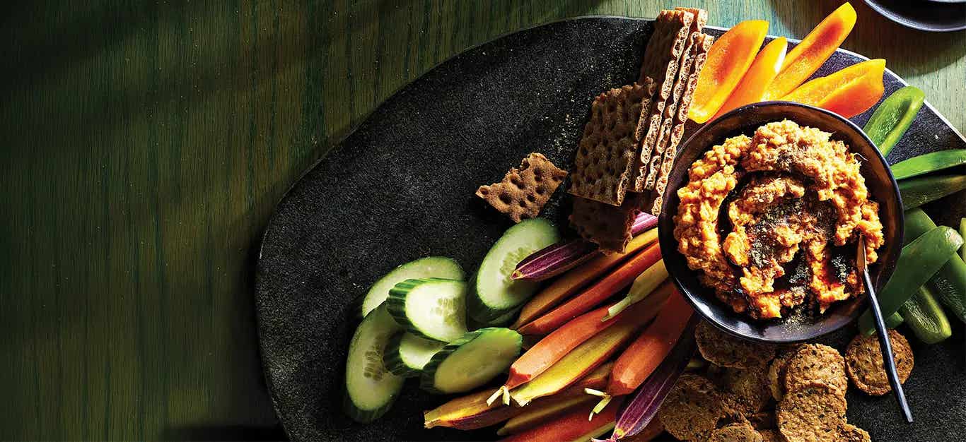 Sweet Potato Tahini Dip with Za'atar on a platter with cucumber, colorful heirloom carrots, and whole grain crackers
