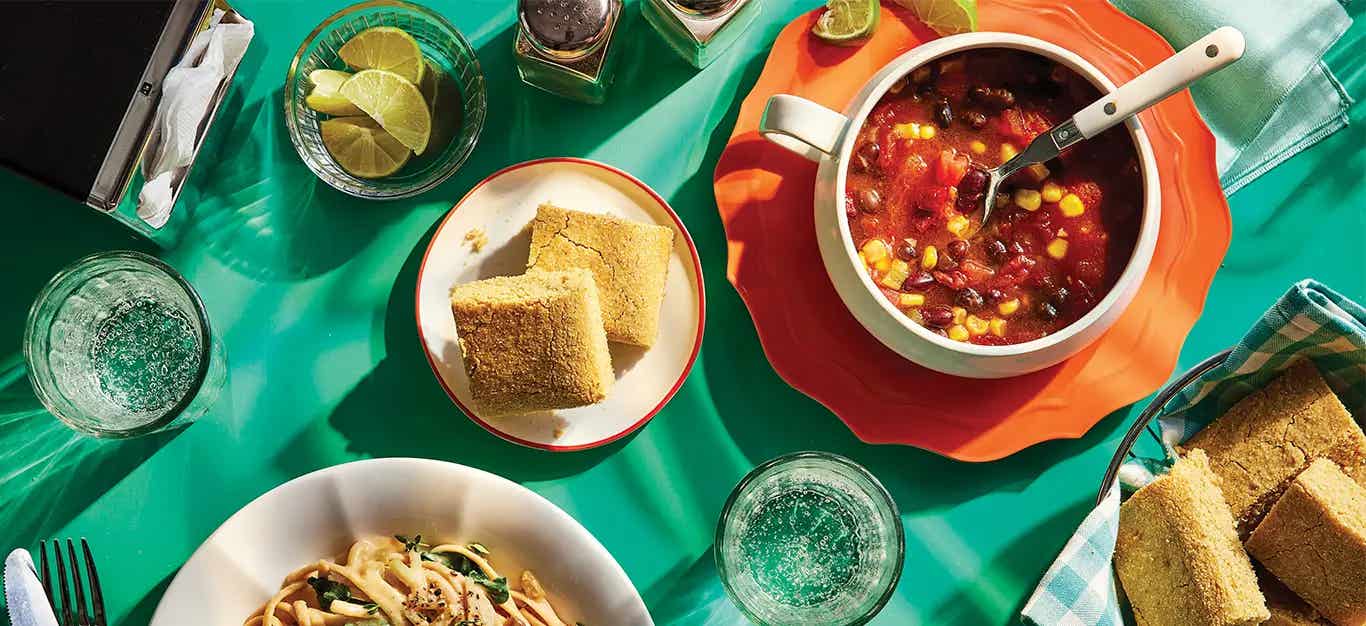 2-Bean Chili in a white bowl on a red plate, next to a small plate with two pieces of cornbread