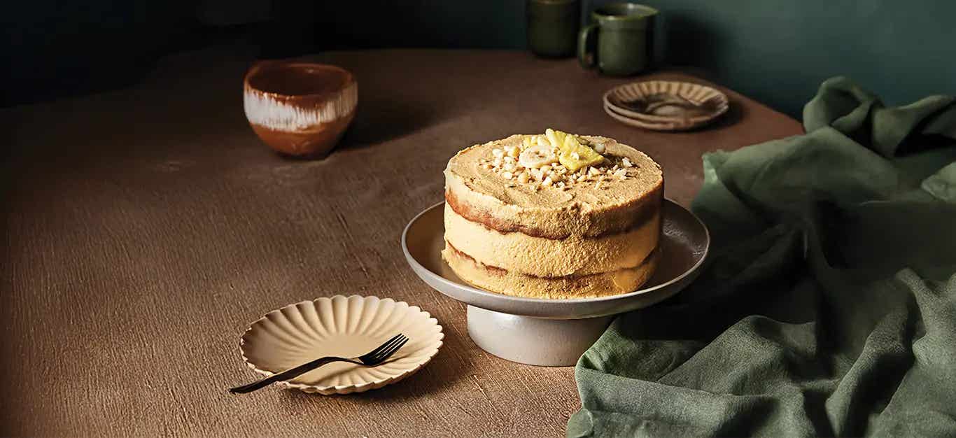 Banana Pineapple Cake with Macadamia Nuts on a cake stand with an empty plate and fork on the side