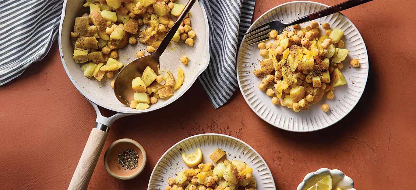 A non-stick skillet of Quick Curried Chickpeas and Potatoes, with some dished up onto two plates
