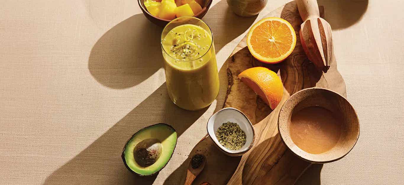 Power Citrus Smoothie next to a chopping board, cut oranges, half an avocado. The sun is streaming in from the side