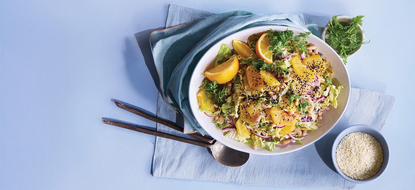 White Bean and Shaved Cabbage Salad with Orange Dressing in white plate on a blue tablecloth