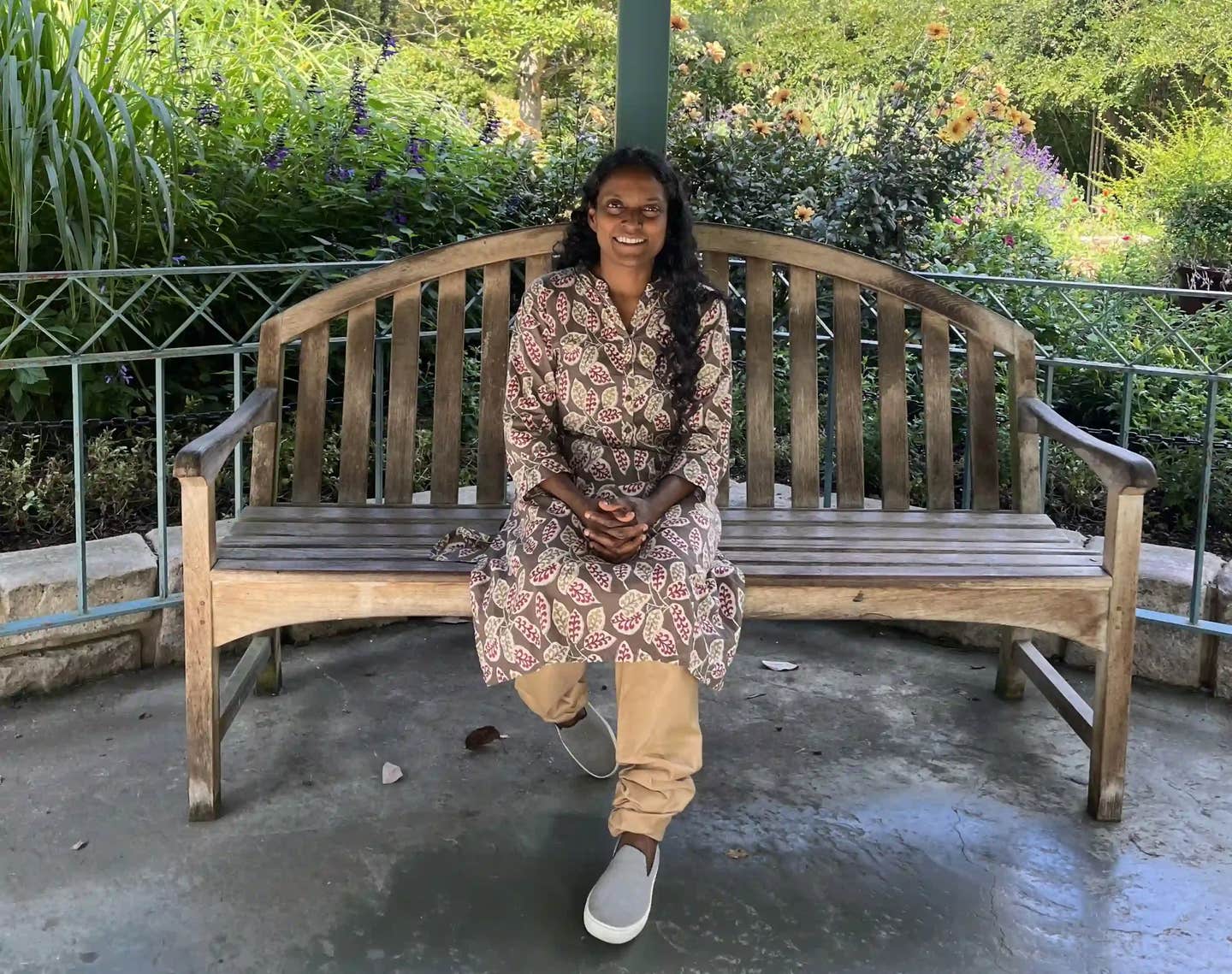 Nurse practitioner Maxine Charles sitting on a bench in a gazebo on a sunny day, wearing a leaf-print dress and khaki pants, smiling, after lowering her A1c on a plant-based diet and reversing prediabetes