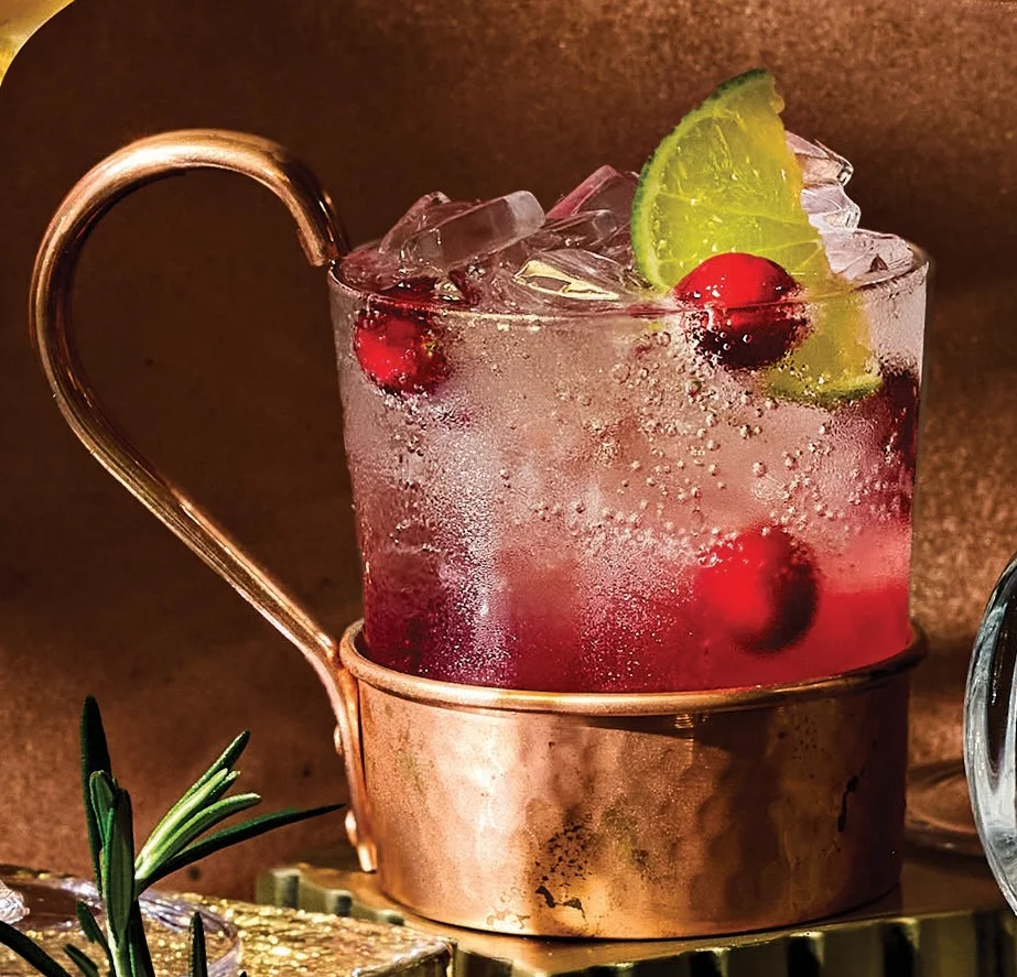 A fizzy cranberry mock mule served in a copper mug filled with ice, garnished with whole cranberries and a lime wedge, with warm-toned lighting.