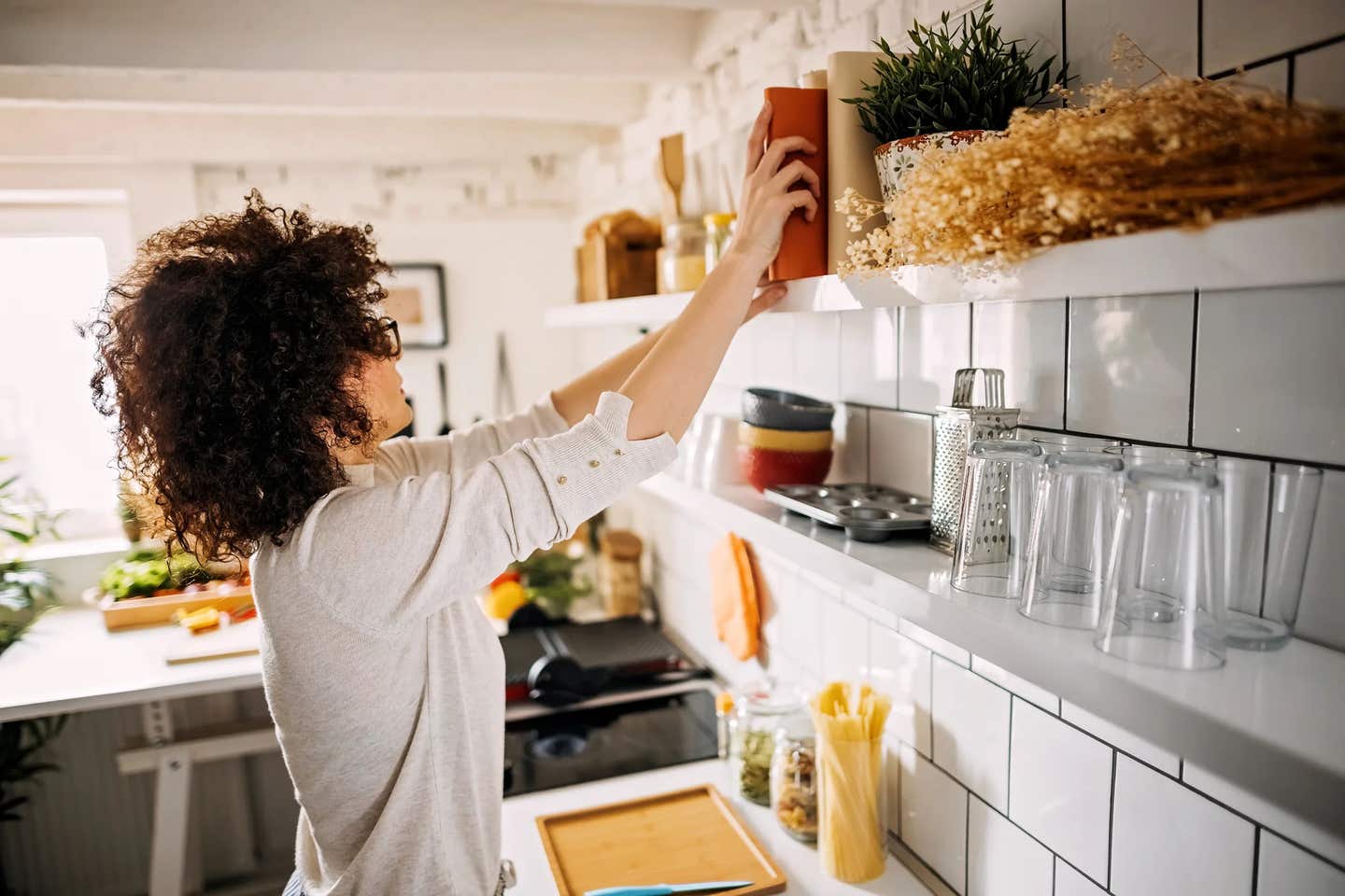 Woman in kitchen reaching for cookbook off shelf