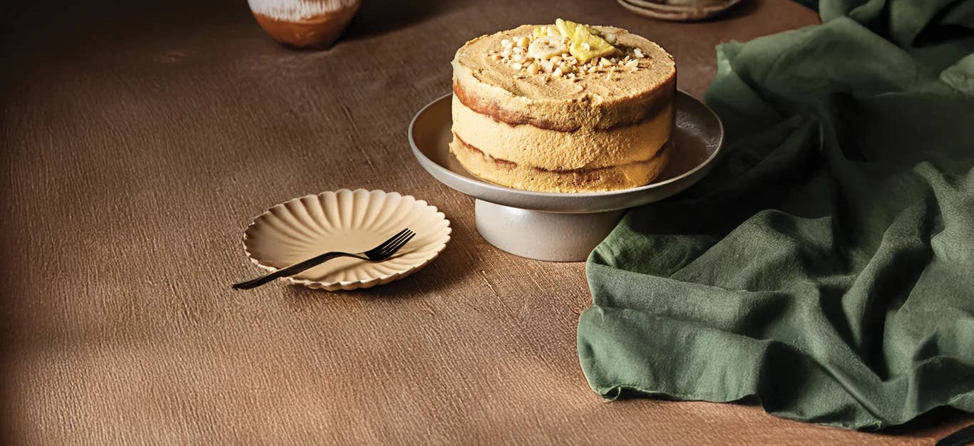 Banana Pineapple Cake with Macadamia Nuts on a cake stand with an empty plate and fork on the side