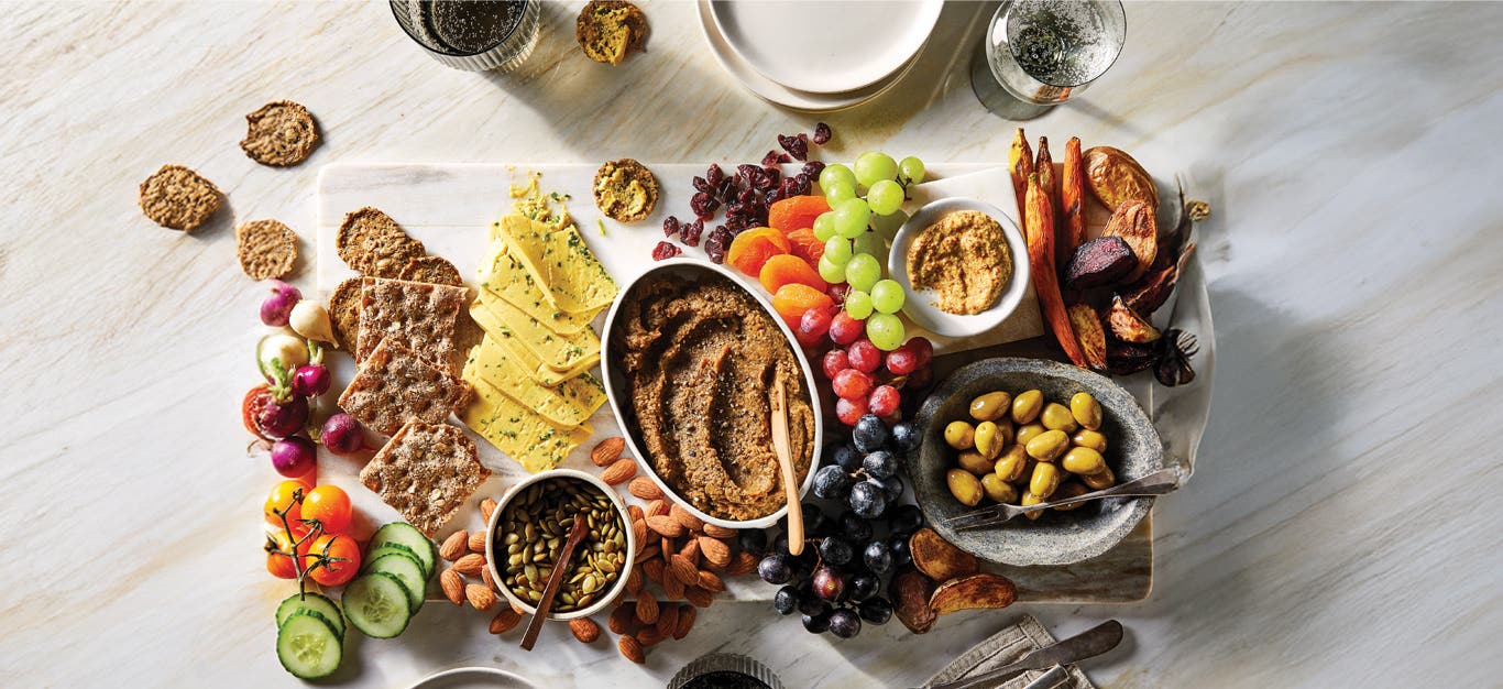 A vegan charcuterie board featuring grapes, olives, nuts, dried fruit, a homemade vegan pate and homemade vegan cheese, and toast