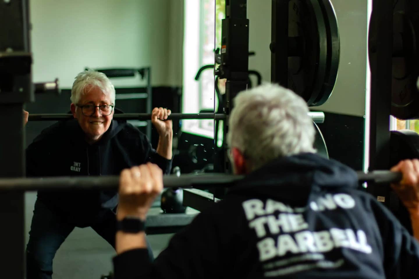 Vegan nun Sister Pat Farrell dead lifts weights in a gym, smiling at herself in the mirror