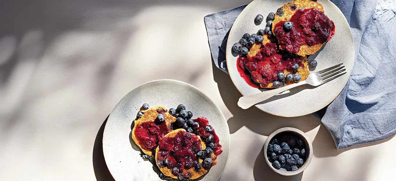 Two whites plates with Quinoa Pancakes drizzled with blueberry sauce