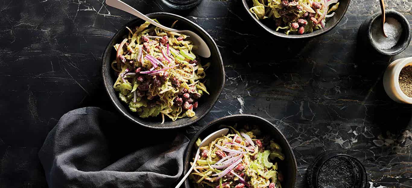 Three bowls of Easy Coleslaw with Red Beans and Rosemary. The bowls are black on a black backdrop so that the bright green and red of the coleslaw pops against the darker colors