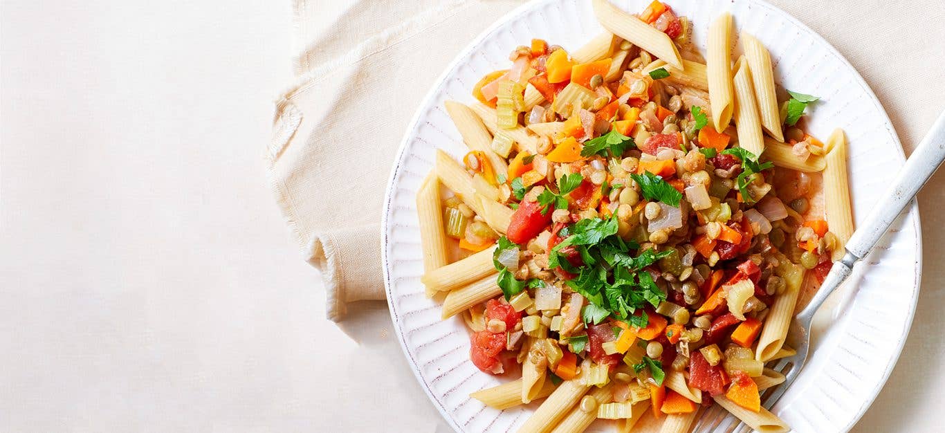 Hearty Lentil Ragu with Penne on a white plate with a metal fork