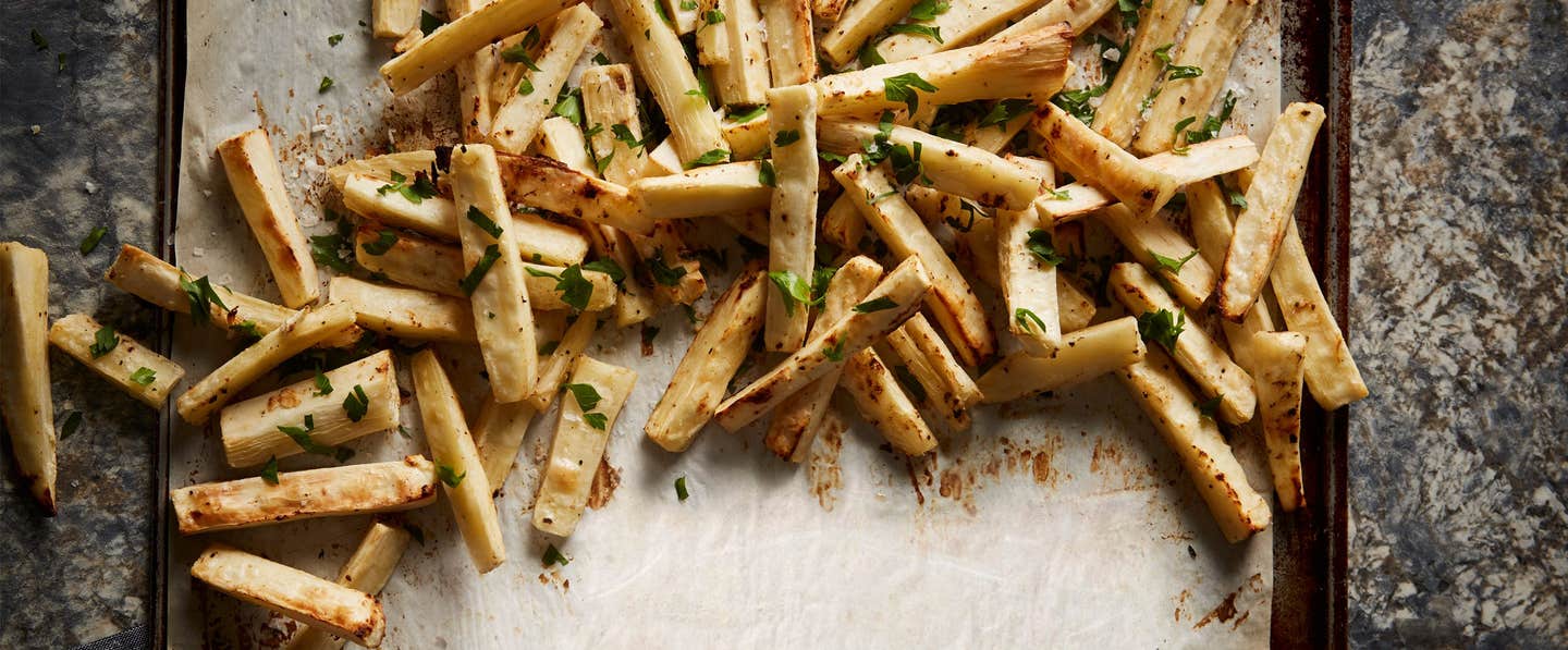 Baked Yuca Fries on sprinkled with chopped fresh herbs, on parchment paper