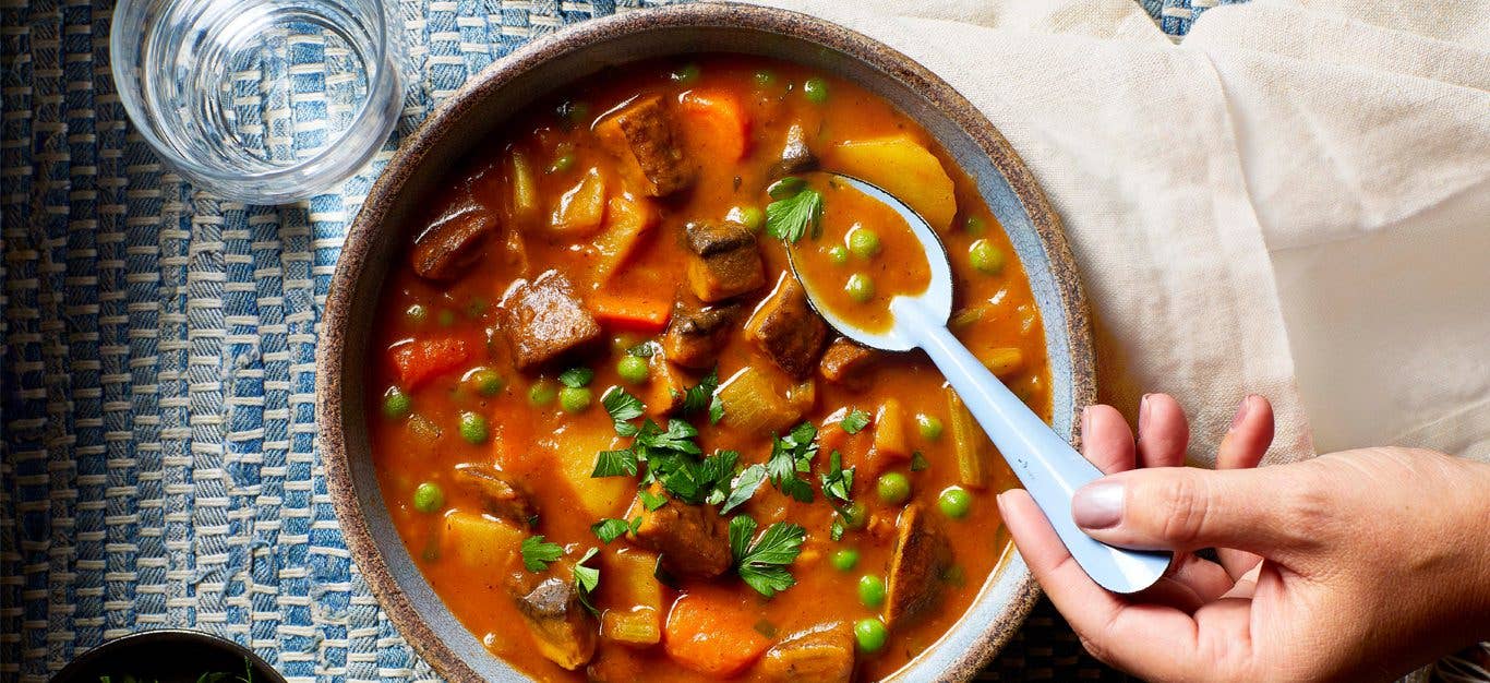 A woman's hand scoop up a spoonful of the Best-Ever Beefless Stew (a Vegan Beef Stew) from a ceramic bowl