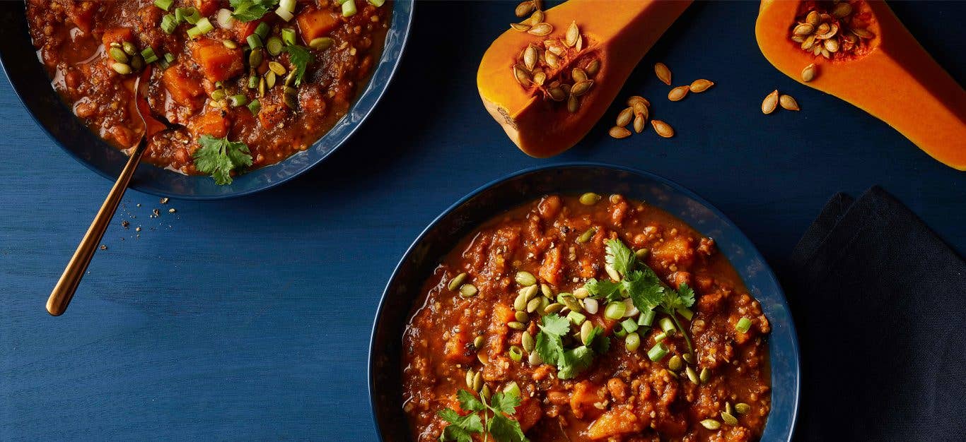 Butternut-Bulgur Chili in blue bowls with quartered butternut squash on the table next to the bowls