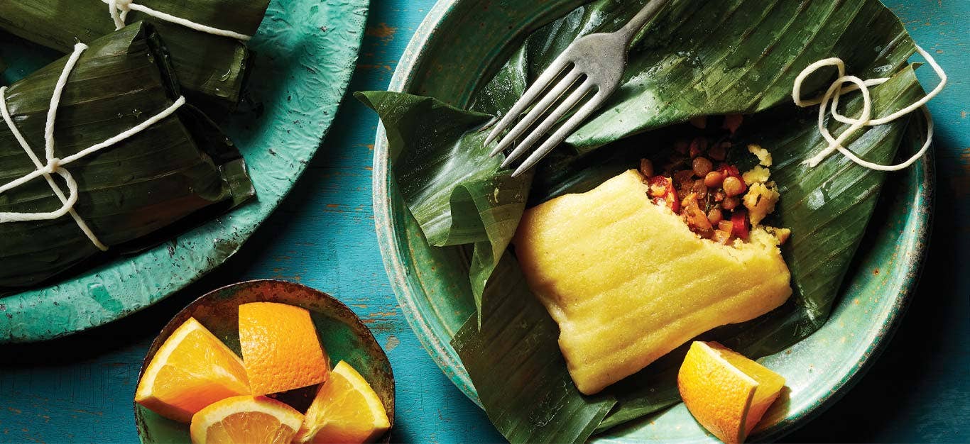 Vegan Pasteles with Lentils in banana leaves on a green wooden plate