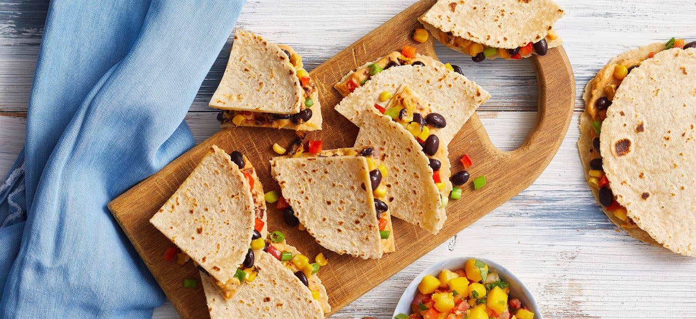 Chipotle Hummus Quesadillas on a wooden serving tray with a bowl of fresh mango salsa