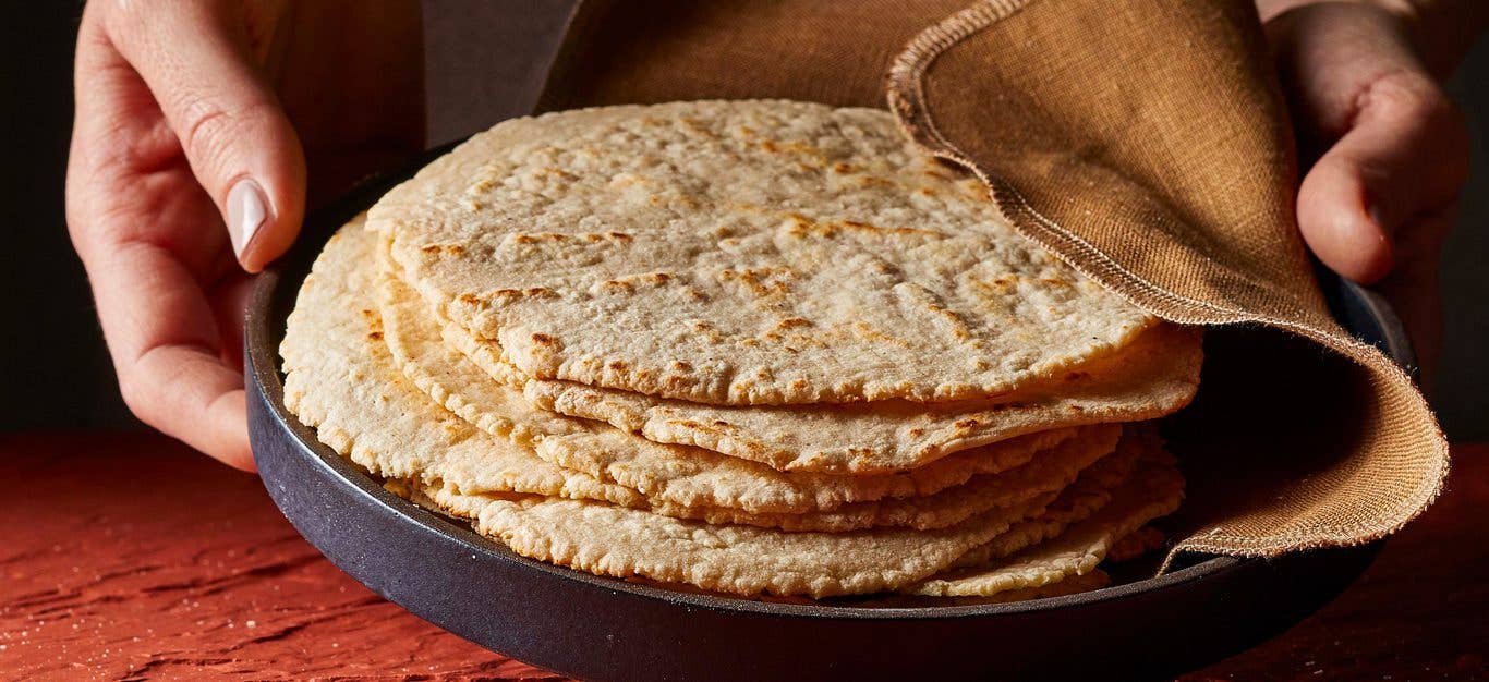 Hands holding a plate of stacked corn tortillas