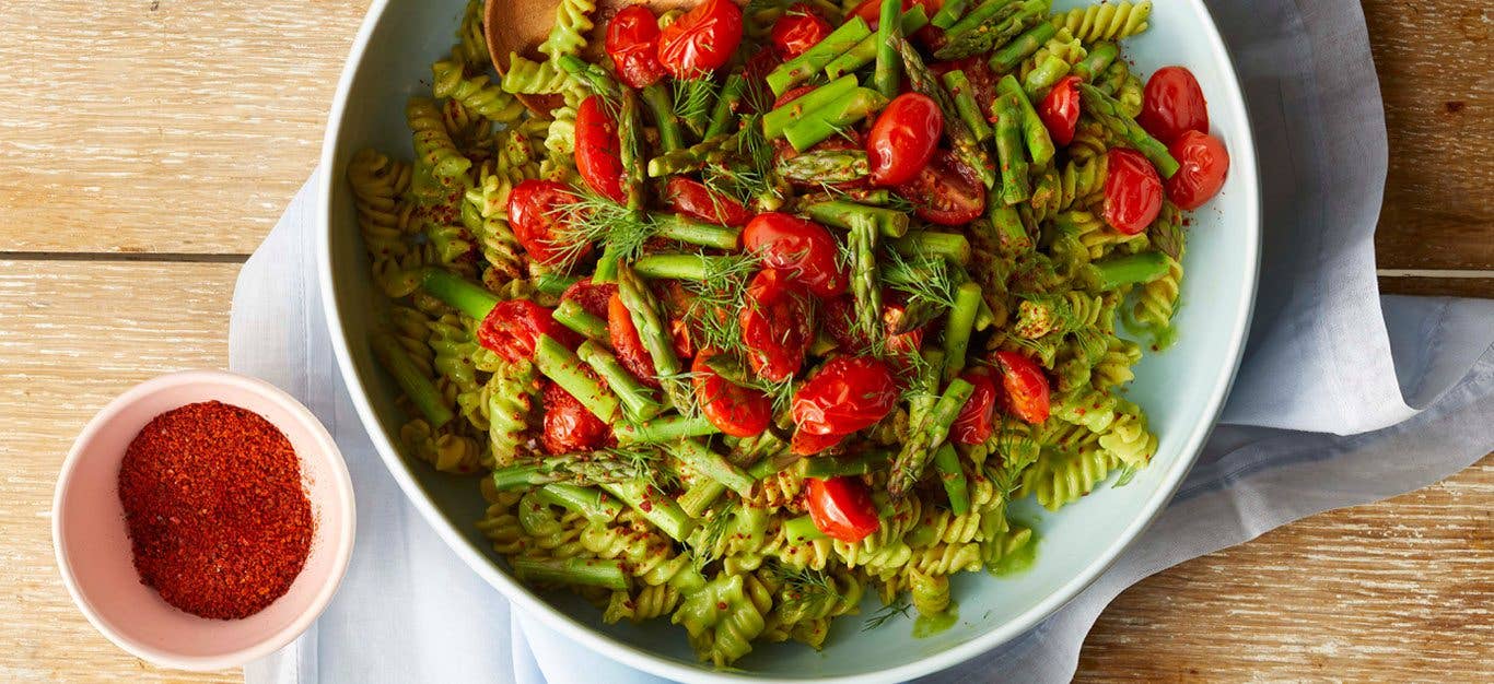 Creamy Avocado Kale Pasta in a white bowl on wooden table next to a small bowl of paprika