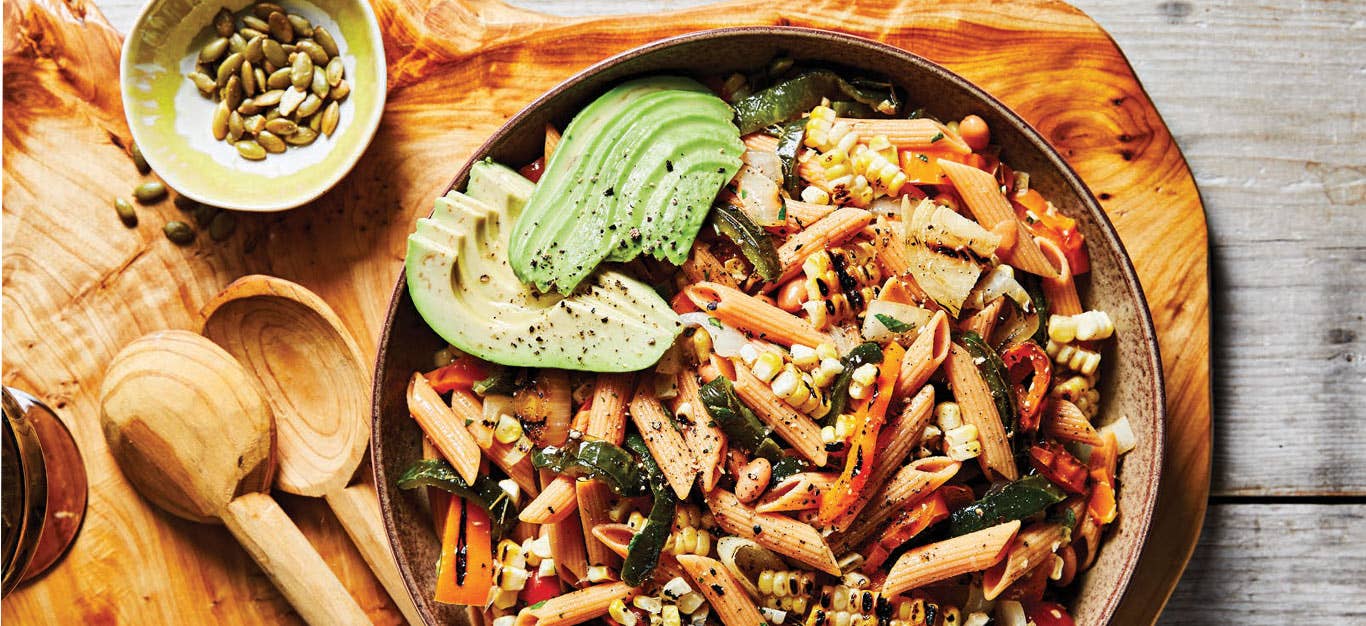 Fajita Pasta Salad in a gray bowl on a wood cutting board with a small bowl of pepitas