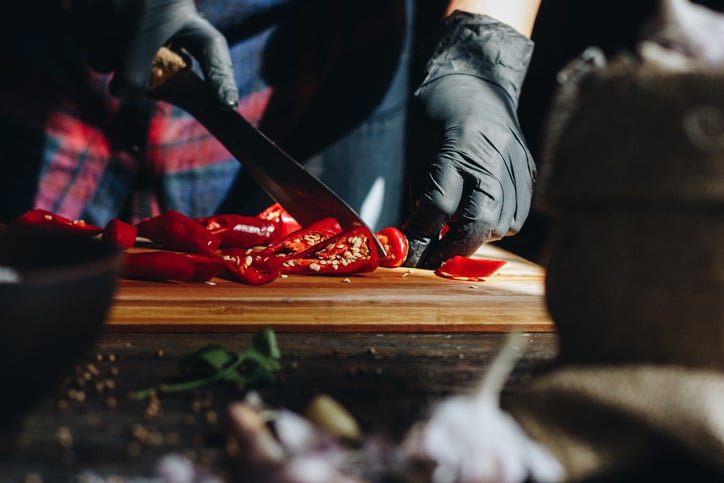 Woman hands in black gloves chopping red hot chili peppers on wooden table