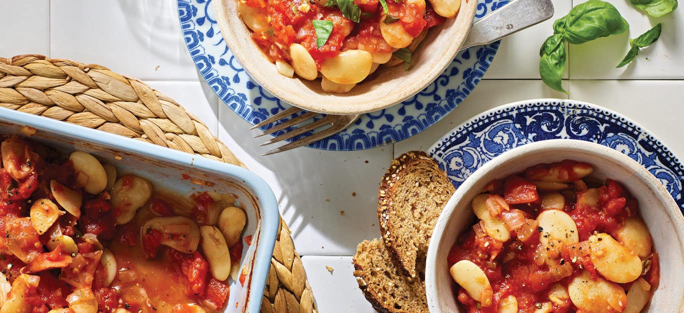 Gigantes Plaki: Greek Lima Beans with Stewed Tomatoes in white bowls placed on white and blue china plates, served with a side of dark bread